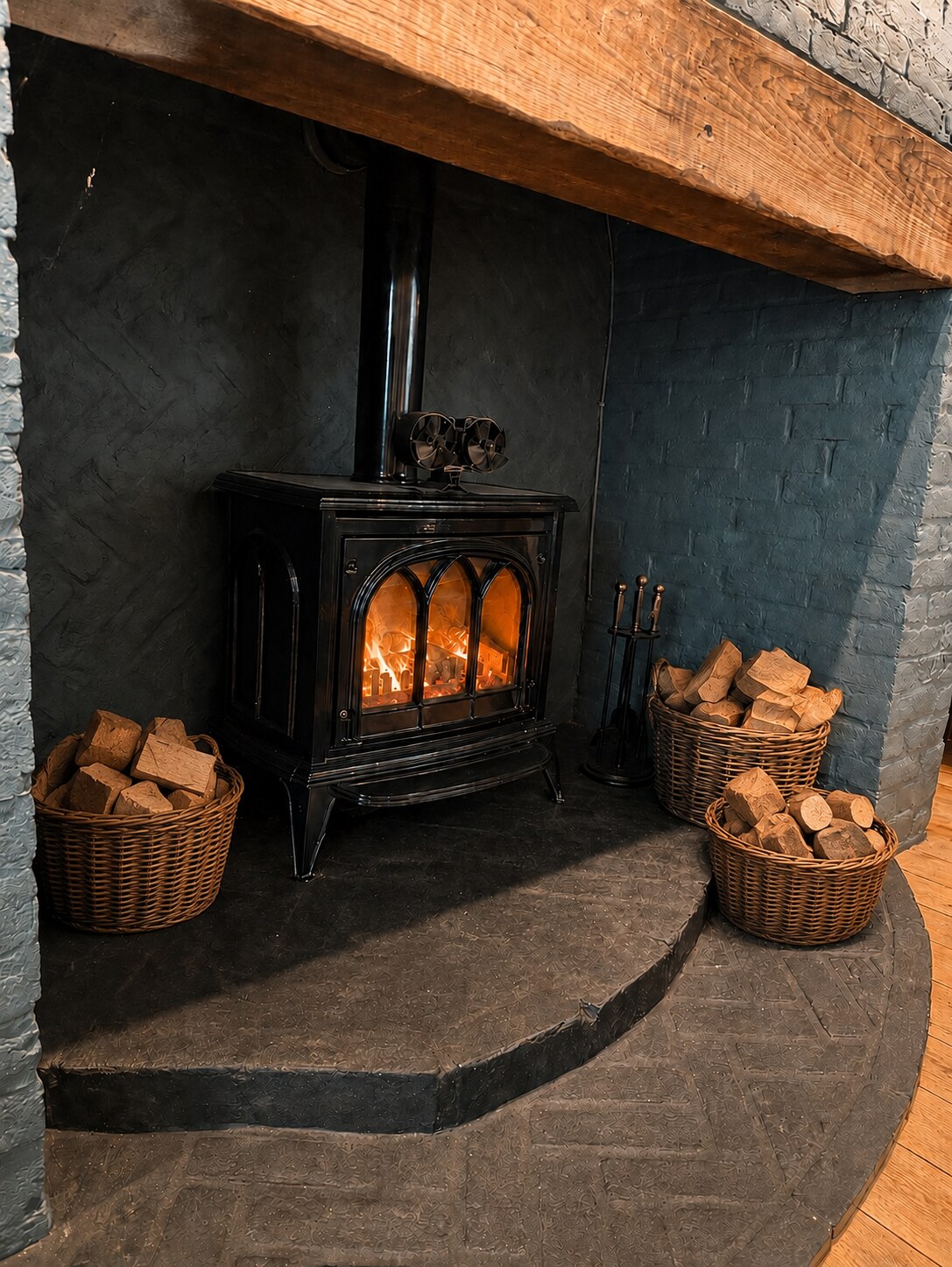 The Pig and Peacock log burner glowing beside three full baskets of logs
